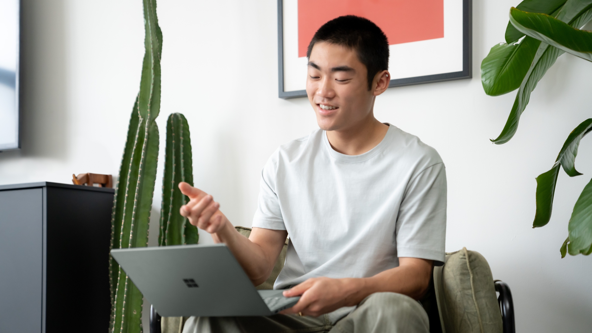 Egy fiatal férfi boldogan használ egy laptopot egy modern szobában, ahol szobanövények vannak.