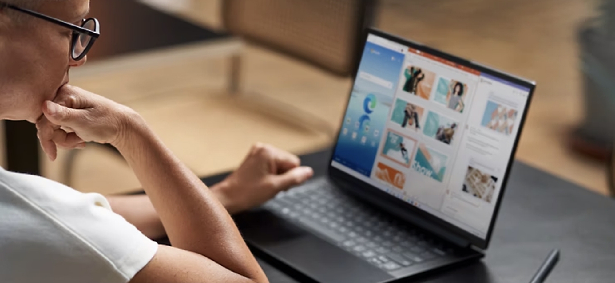 Person in glasses using a laptop displaying colorful website graphics, seated at a wooden table.