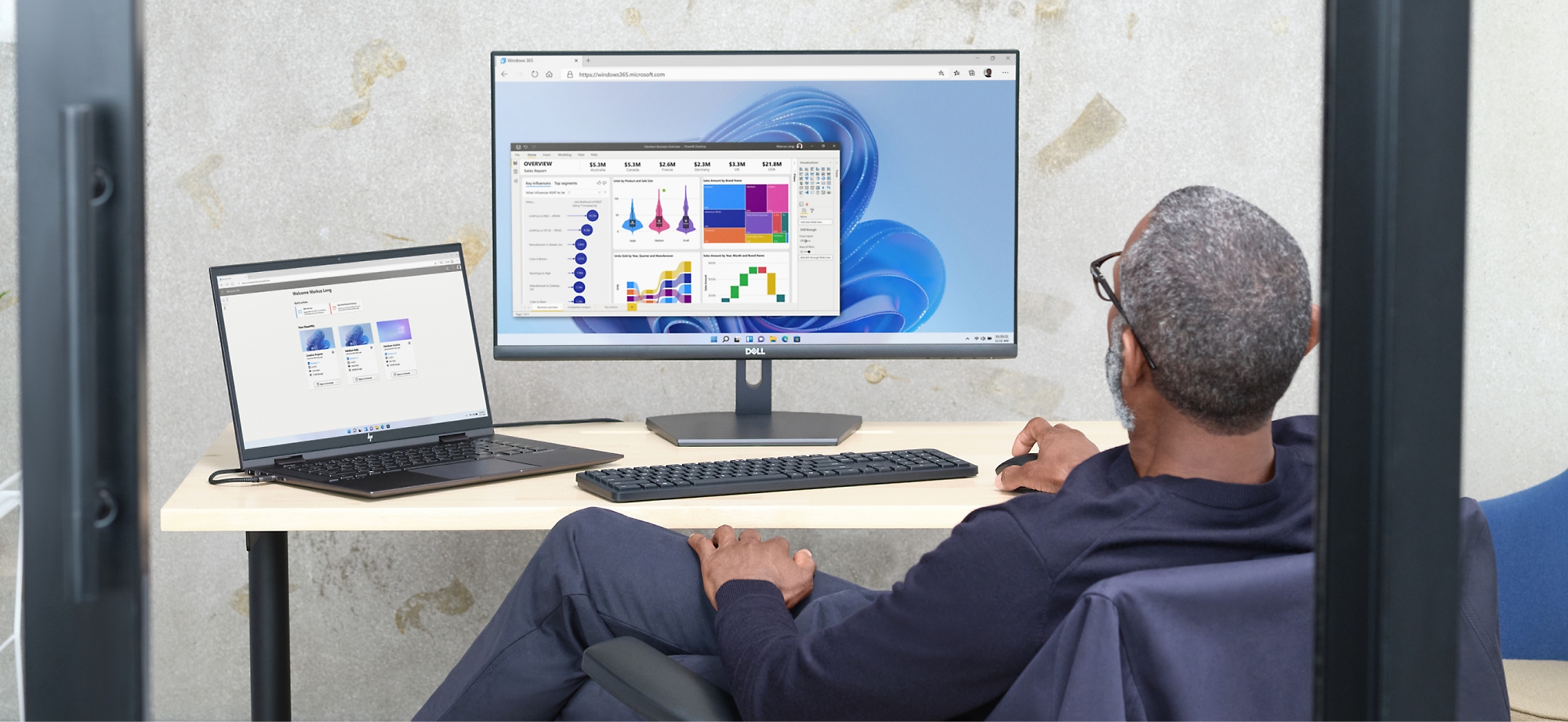 A man reviews data charts on a computer screen and laptop in an office setting.