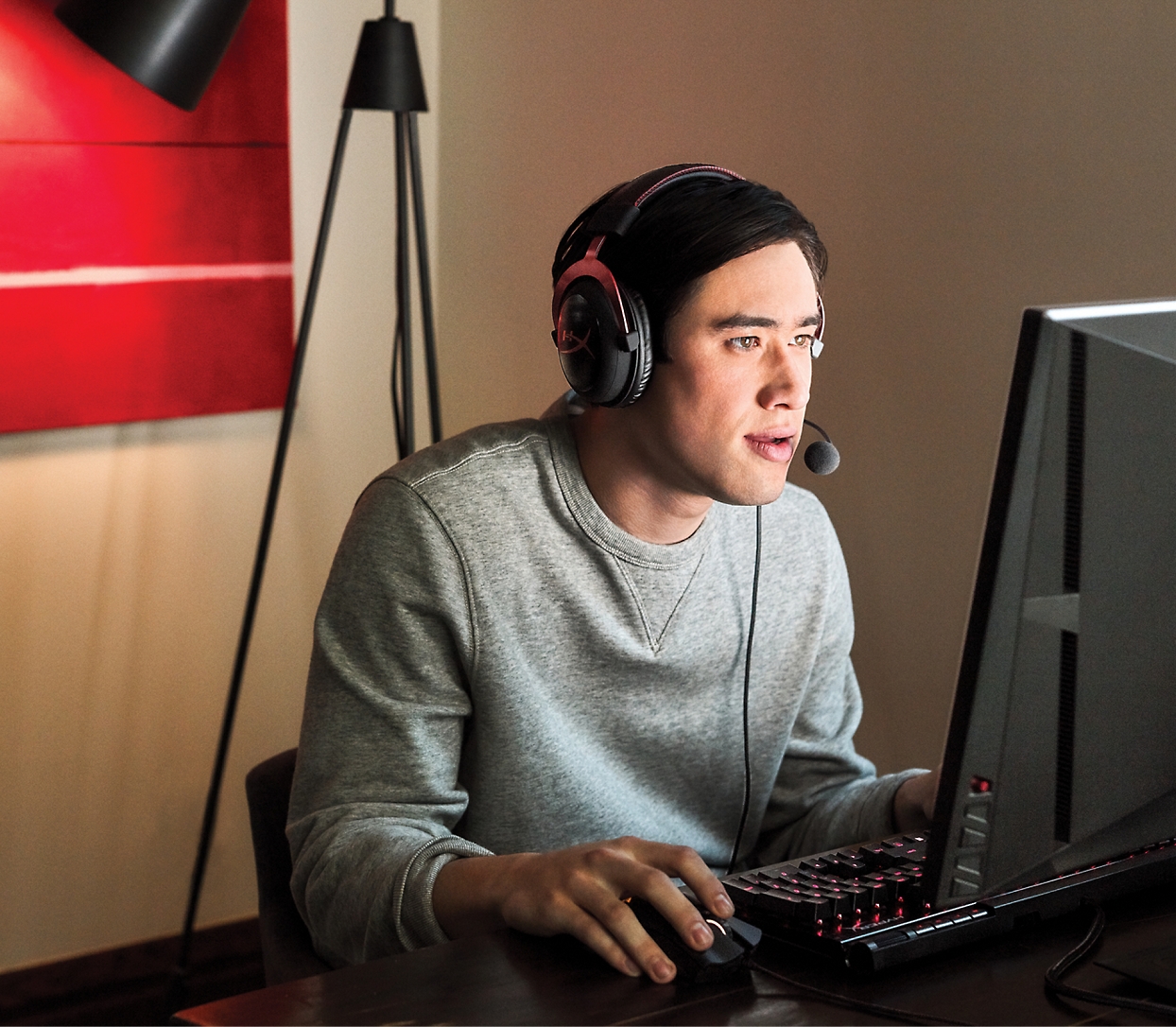 A person wearing headphones with a microphone uses a desktop computer in a dimly lit room, concentrating on the screen.