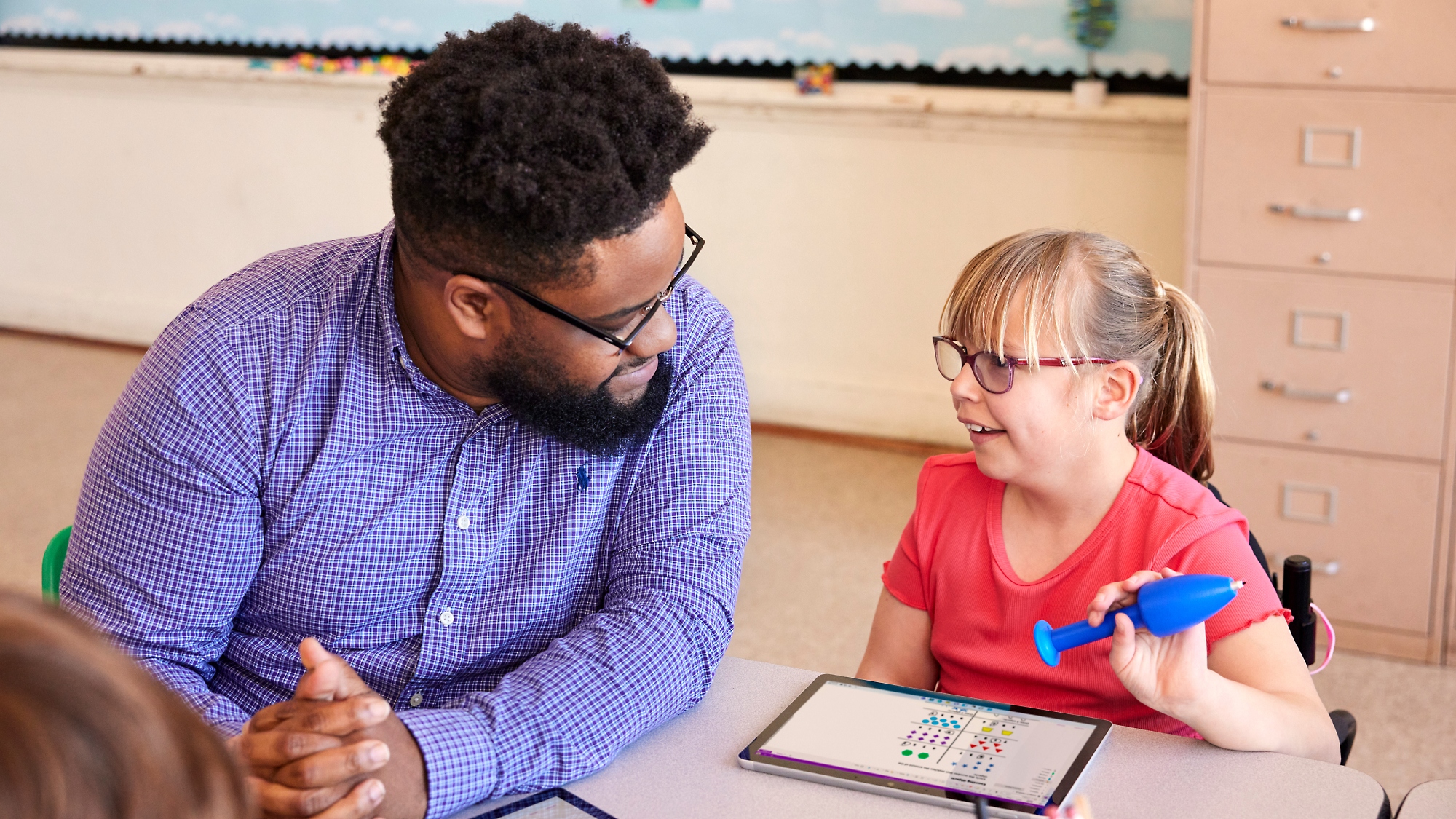 A person and a child sitting at a table working on tablet