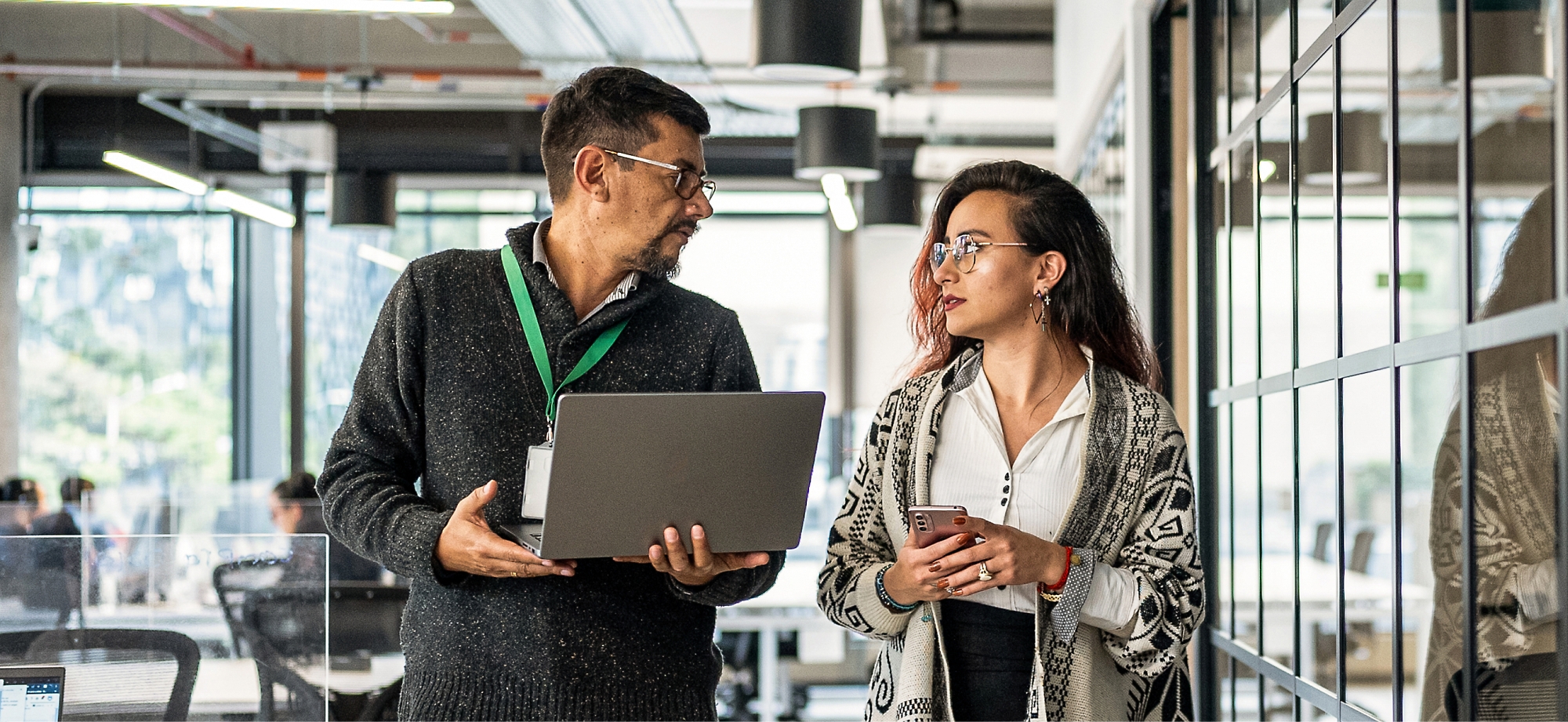 A person and another person standing in a room with a computer and phone