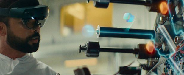 Un hombre con gafas de realidad aumentada trabaja en un brazo robótico complejo con elementos digitales flotantes a su alrededor.