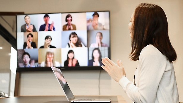 Kvinne presenterer for kolleger via en videokonferansesamtale vist på en stor skjerm på et moderne kontor.