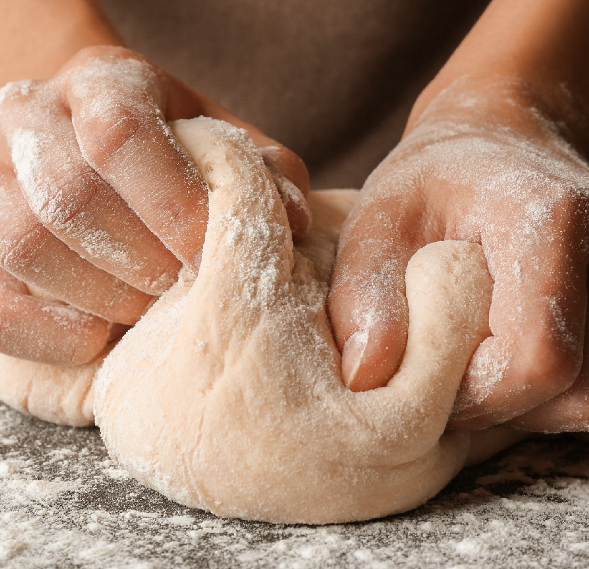 Close-up of hands kneading dough on a floured surface.