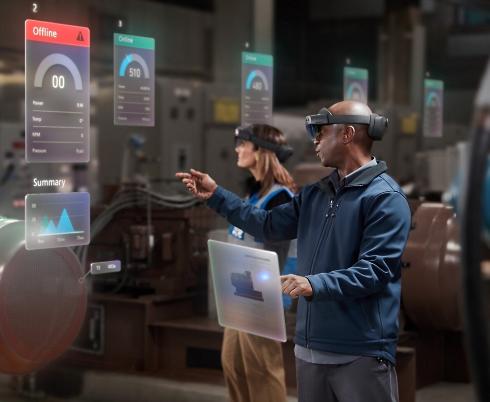 Two individuals using augmented reality headsets to interact with virtual data displays in an industrial environment.