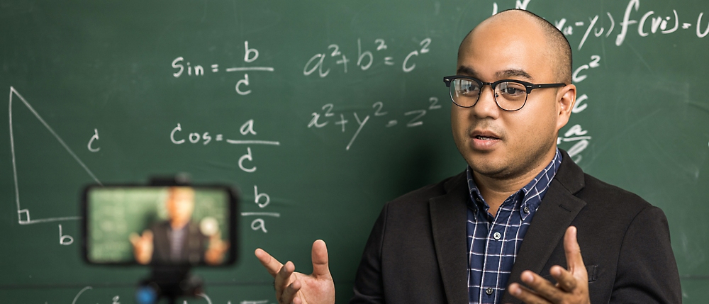 A person in a suit pointing at a chalkboard