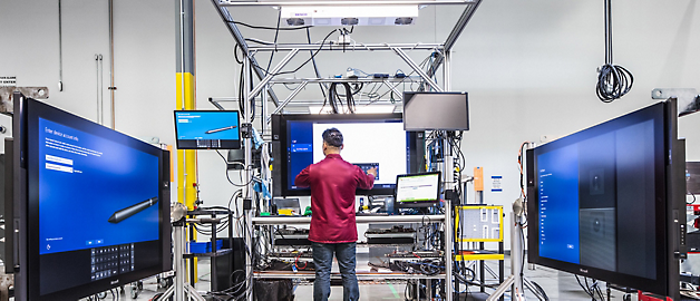 En tekniker arbejder på udstyr i et højteknologisk laboratoriemiljø omgivet af store skærme.