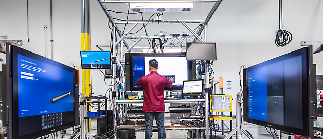 Un técnico trabaja con equipos en un laboratorio de alta tecnología rodeado de monitores grandes.