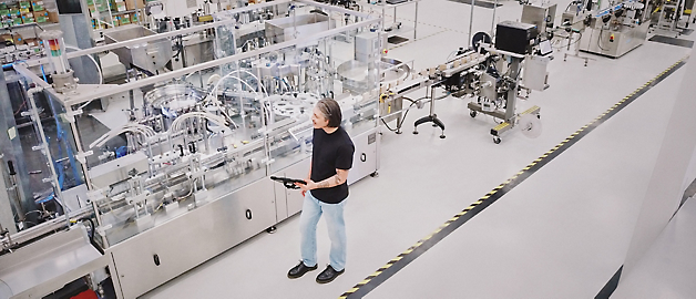 En person står og observerer en automatiseret produktionslinje i en ren og moderne produktionsanlæg.