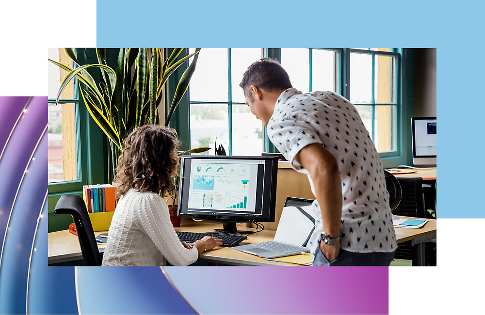 Twee collega's op kantoor, een man en een vrouw, bespreken gegevens op een computerscherm in een helder kantoor met planten.