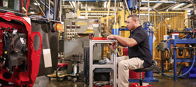 A worker inspects a component at an industrial manufacturing station.