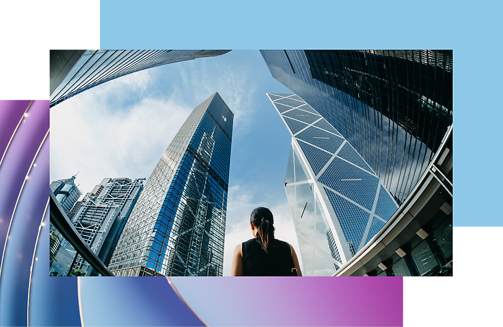 A woman looking up at towering modern skyscrapers under a clear blue sky.