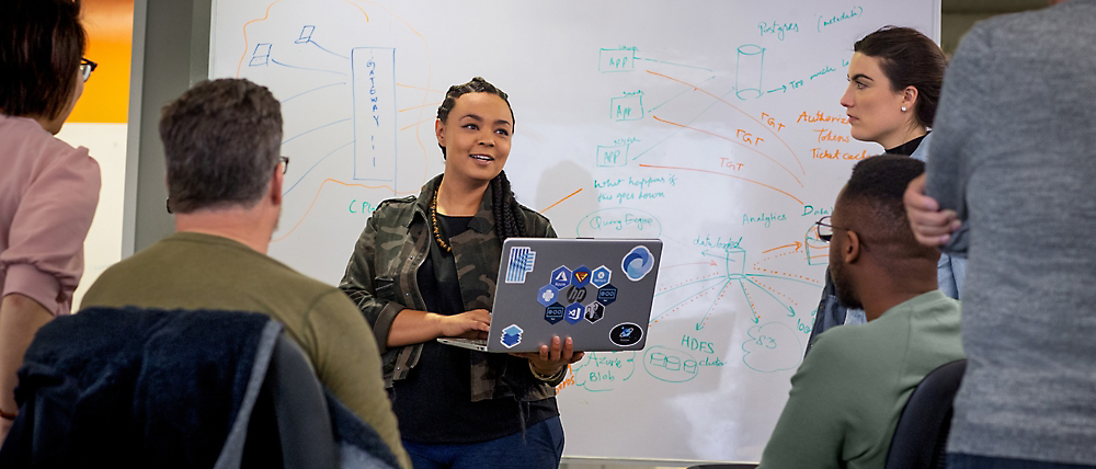 Een vrouw presenteert digitale afbeeldingen op een laptop aan een groep geïnteresseerde collega's in een vergaderruimte