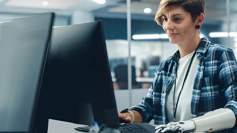 En kvinne med armprotese som jobber konsentret på en datamaskin i et moderne kontormiljø.
