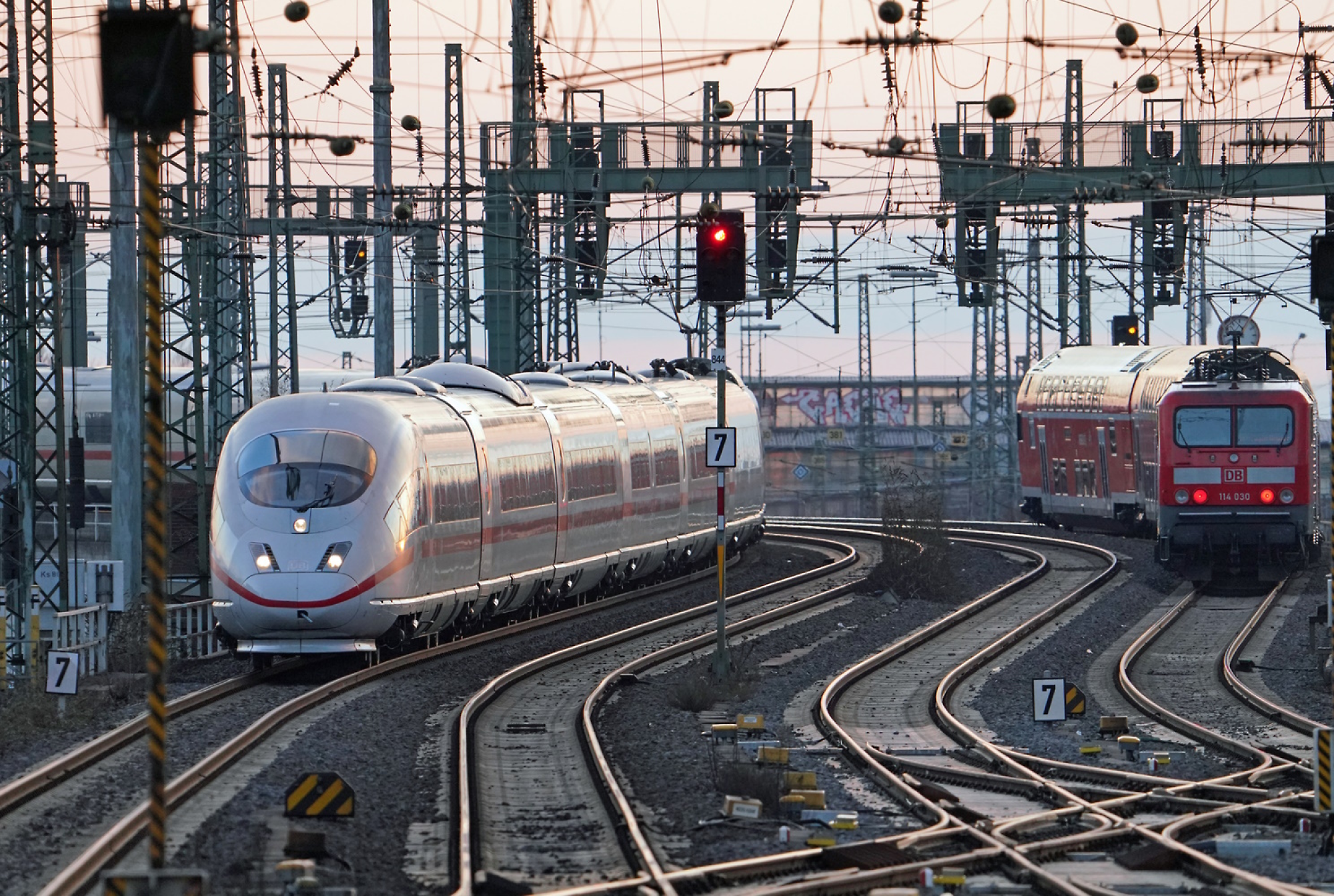 รถไฟความเร็วสูงสมัยใหม่มาถึงสถานีที่มีรางรถไฟหลายรางและสายไฟเหนือศีรษะในเวลาพลบค่ำ