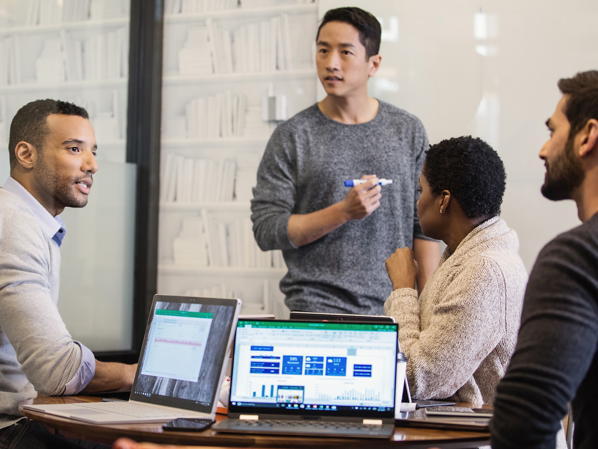 A diverse group of four professionals engaged in a meeting around a table with laptops displaying graphs,