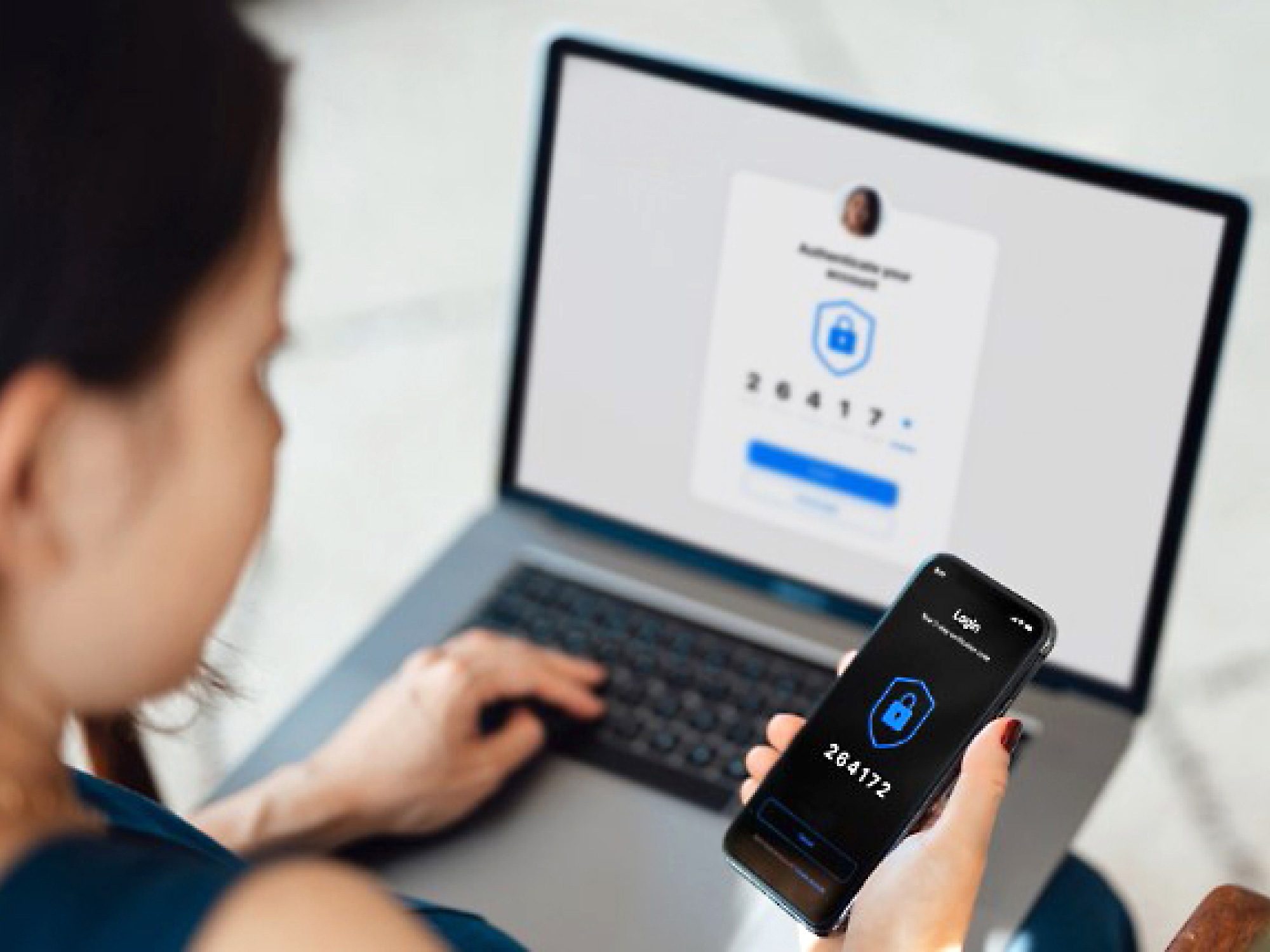 En kvinne med en bærbar datamaskin taster inn en engangskode hun har mottatt på mobilen for sikker pålogging.