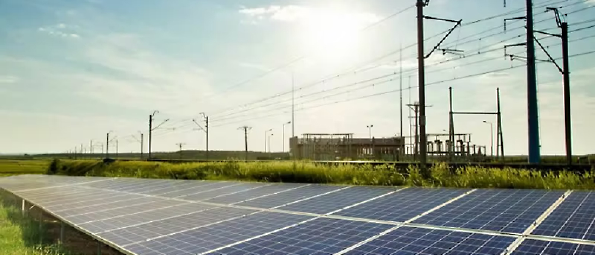 A solar panel array is installed near a power line infrastructure under a clear sky