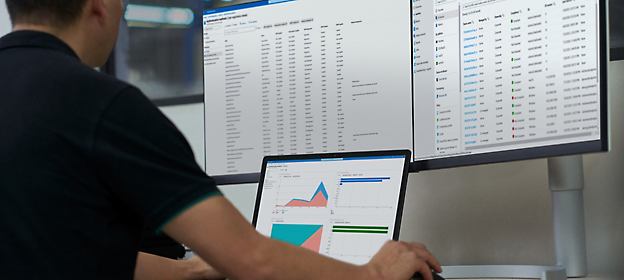 Una persona trabaja en un portátil con gráficos de análisis de datos en pantalla, delante de un monitor más grande 