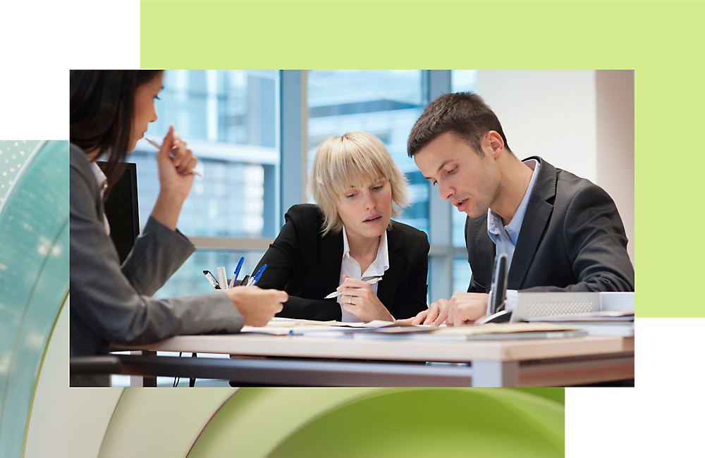 Two professionals, a man and a woman, focused on reviewing document another woman sits beside, listening.