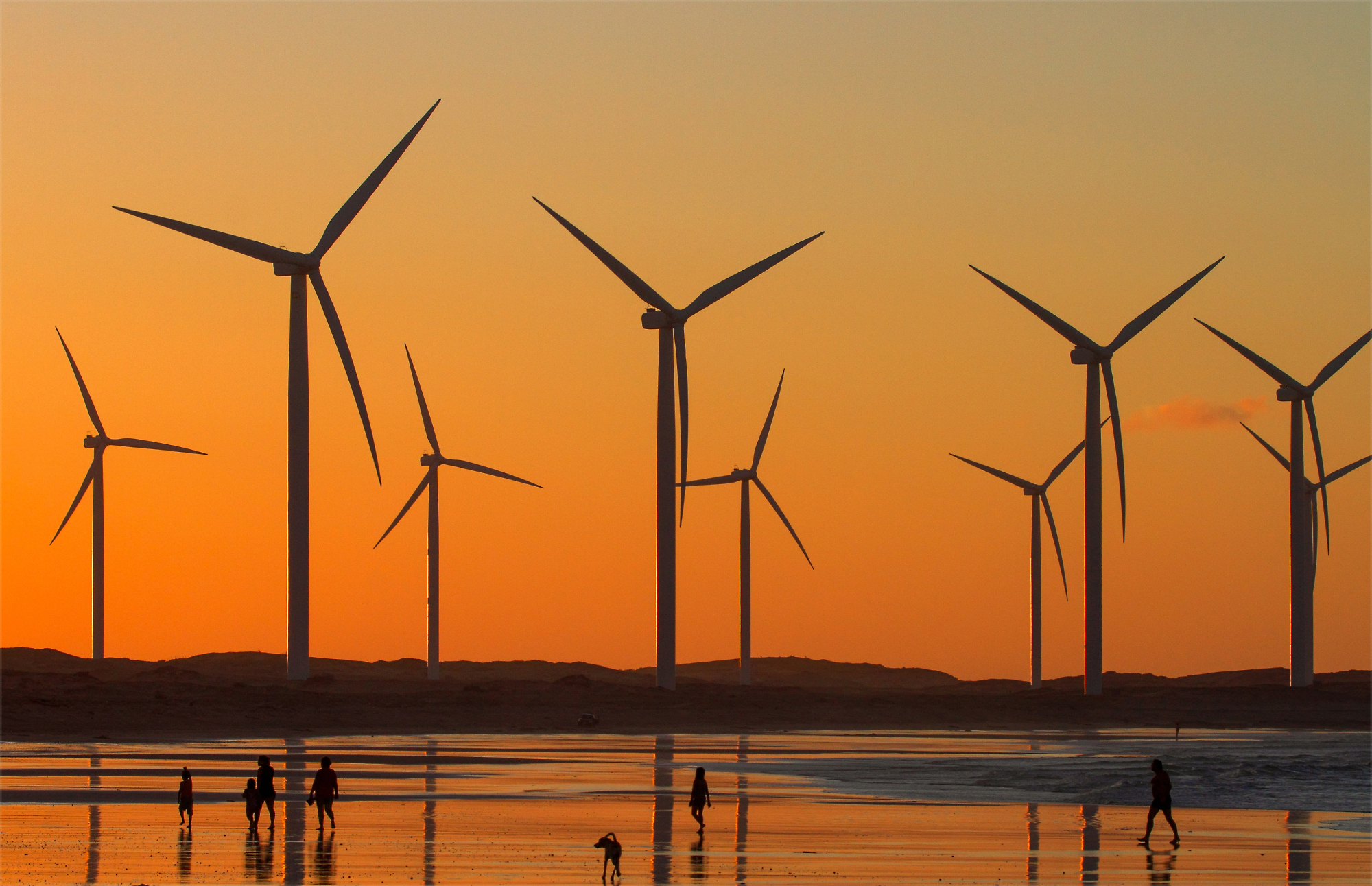 Several wind turbines stand tall against an orange sky during sunset