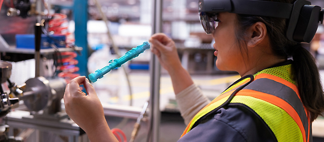 A worker wearing a safety vest and augmented reality glasses inspects an industrial component.