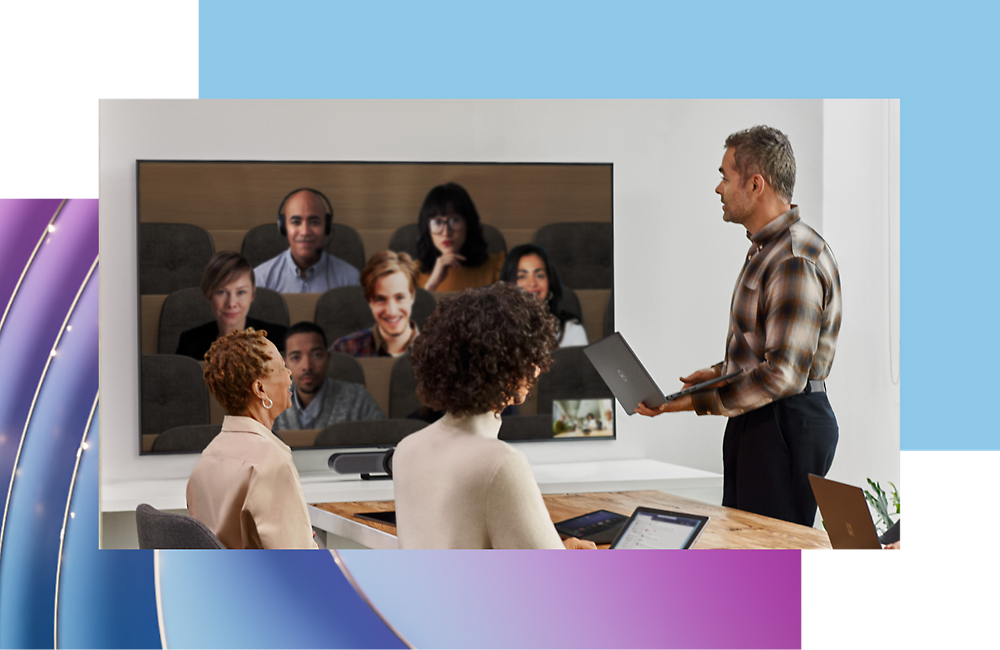 A man presents to colleagues in front of a screen displaying a video call with six other participants.