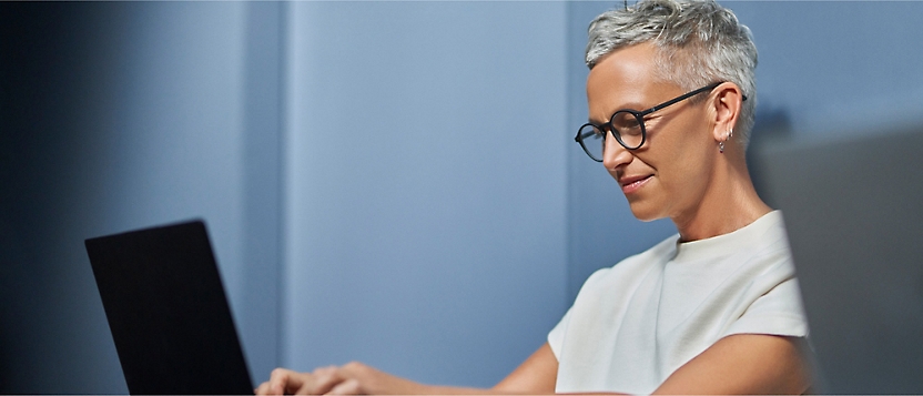 A woman wearing glasses is focused on typing on her laptop.