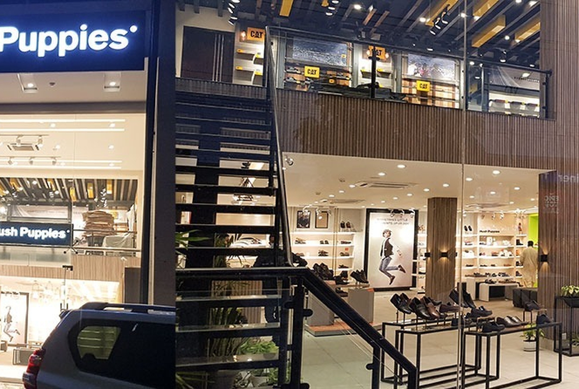 A storefront of a hush puppies store in an urban setting at night, with a customer exiting and an illuminated sign above.