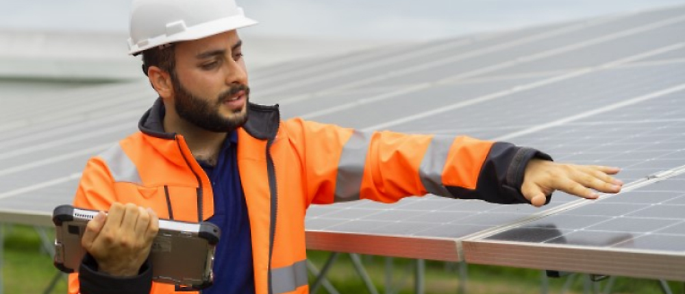 Eine Person in einer orangefarbenen Weste, die auf ein Solarpanel zeigt