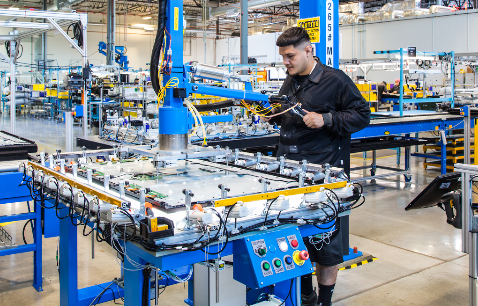 A worker operates a robotic machine in a brightly lit manufacturing facility.