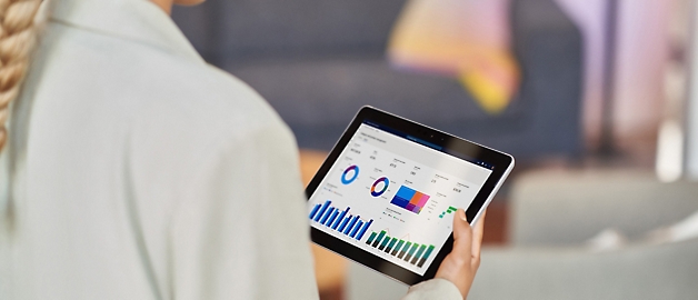 Businesswoman using a tablet displaying colorful graphs and charts, indicating data analysis in an office setting.