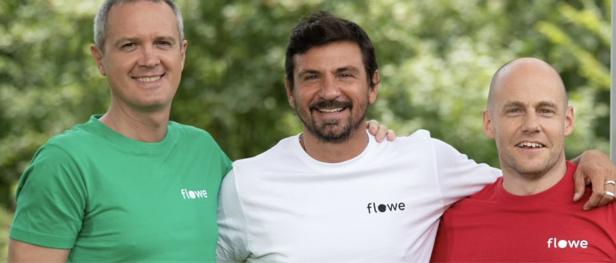 Three smiling men standing outdoor wearing t-shirts in green, white, and red with the logo "flowe" on them