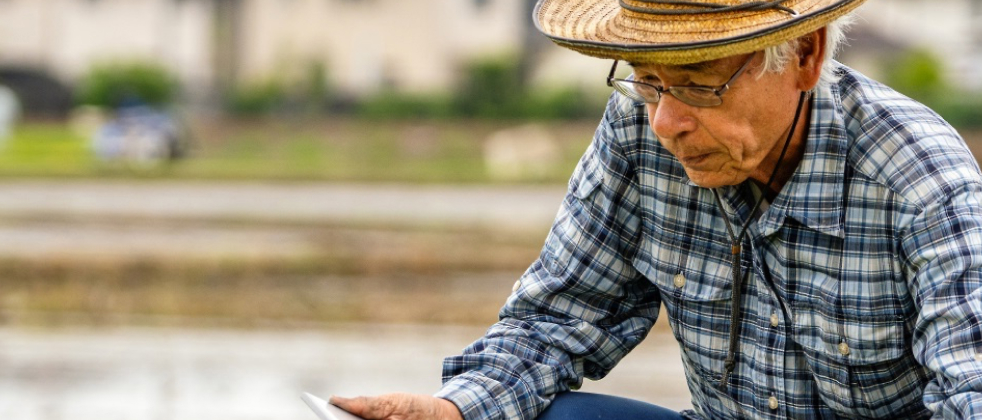 An elderly person closely examining a tablet screen in a rural setting.