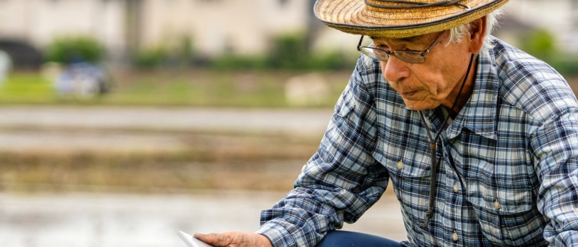 Orang lanjut usia memeriksa layar tablet dengan cermat di area pedesaan.