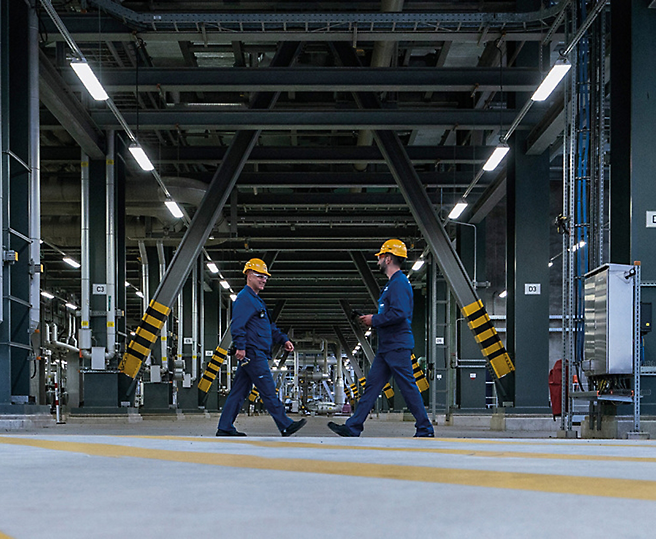 To medarbejdere i sikkerhedshjelme, der går gennem en industriel facilitet.