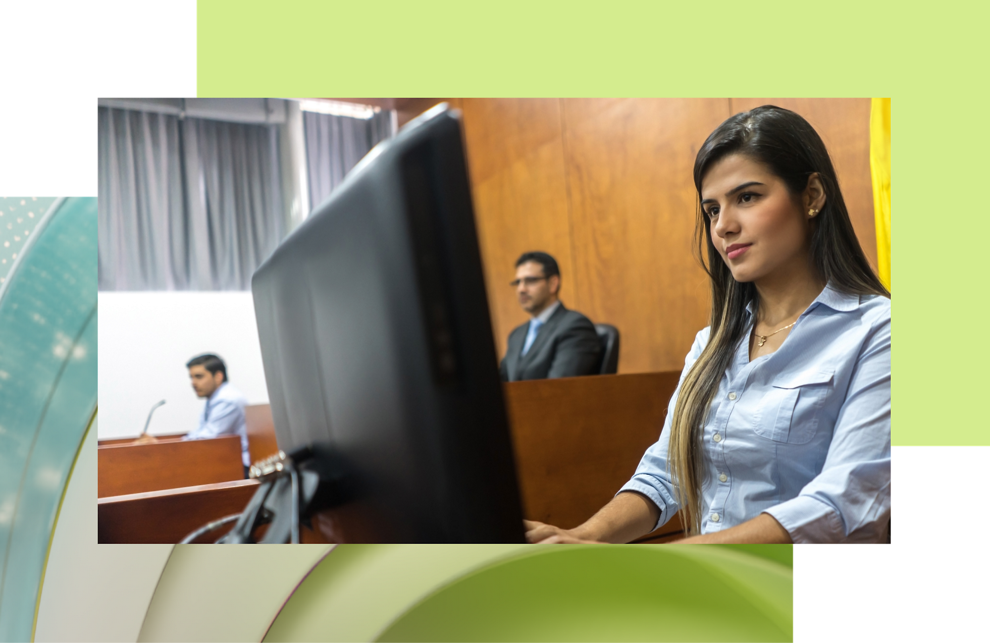 صورة لشابة ترتدي قميصاً أزرق تجلس على مكتب مع جهاز كمبيوتر في قاعة المحكمة؛ رجلان في الخلفية