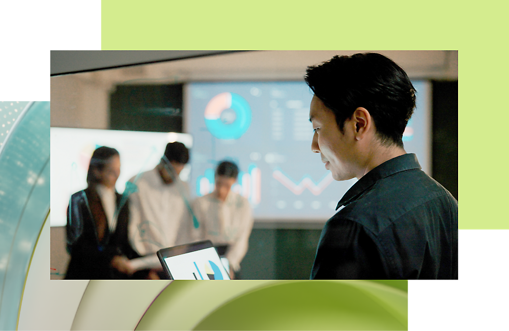 Ein Geschäftsmann, der ein Tablet benutzt, während seine Kollegen Daten auf einem digitalen Bildschirm im Hintergrund besprechen.