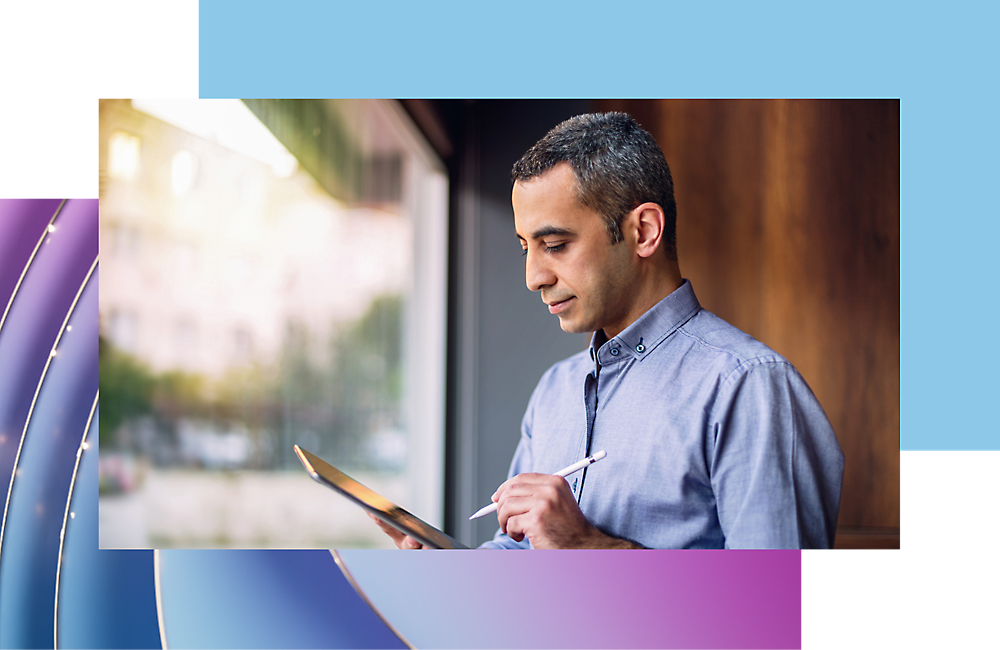 A man in a blue shirt using a tablet near a window, focused on his task.