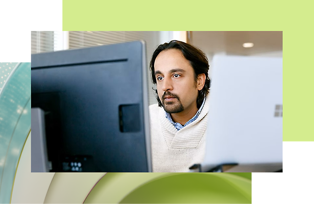 A man with medium-length hair working intently at his computer in an office environment.