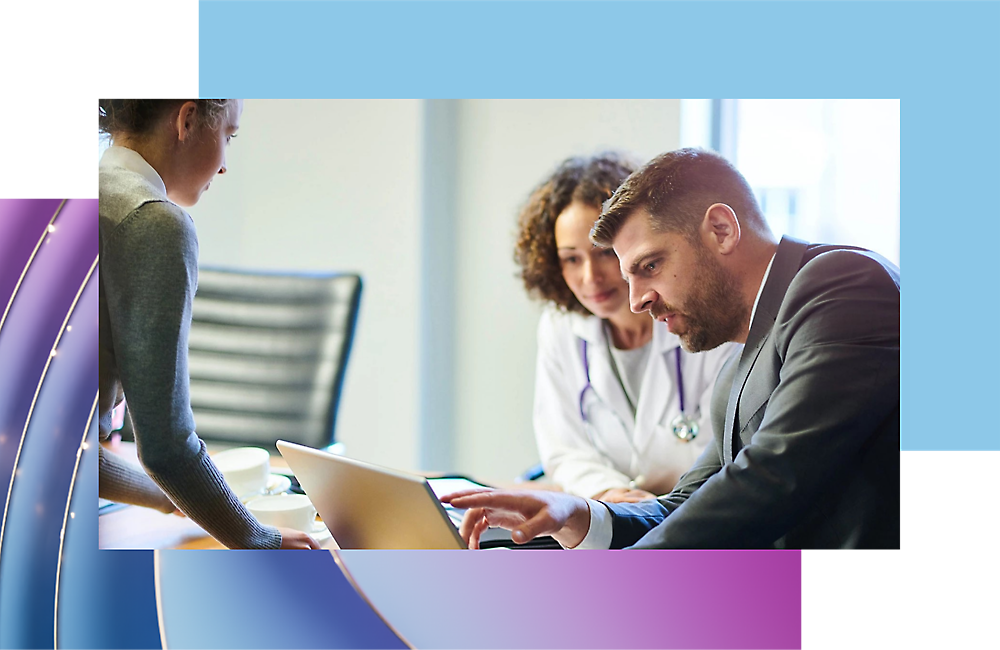 Three professionals in a meeting, one man and two women, discussing over a laptop in a bright office setting.