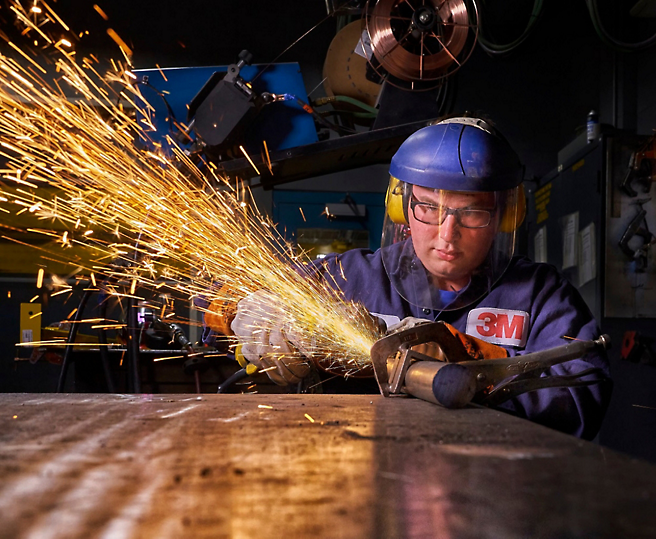 En svejser i beskyttelsesudstyr fokuserer på sit arbejde samtidig med der flyver gnister fra metallet, som han er ved at slibe.