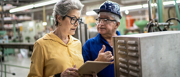 Senior fabrikstilsynsførende med tablet diskuterer produktionsoplysninger med en medarbejder.