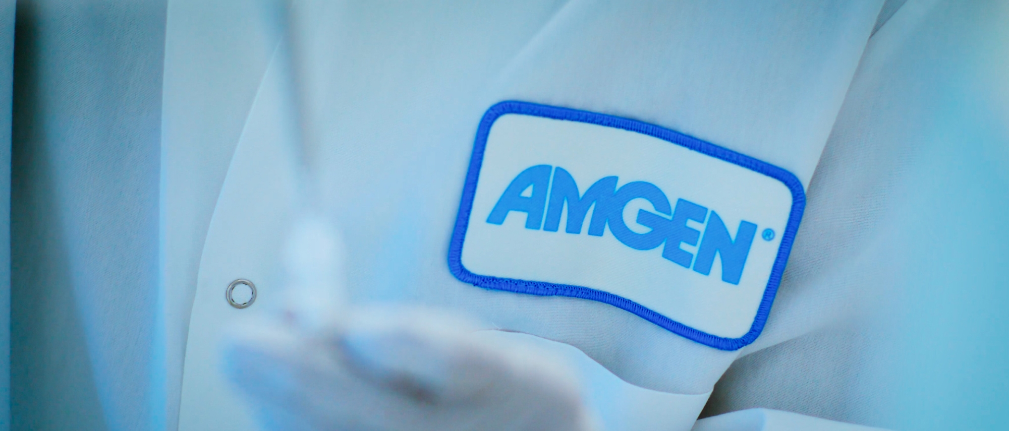 Close-up of a person wearing a white glove and logo of Amgen on shirt