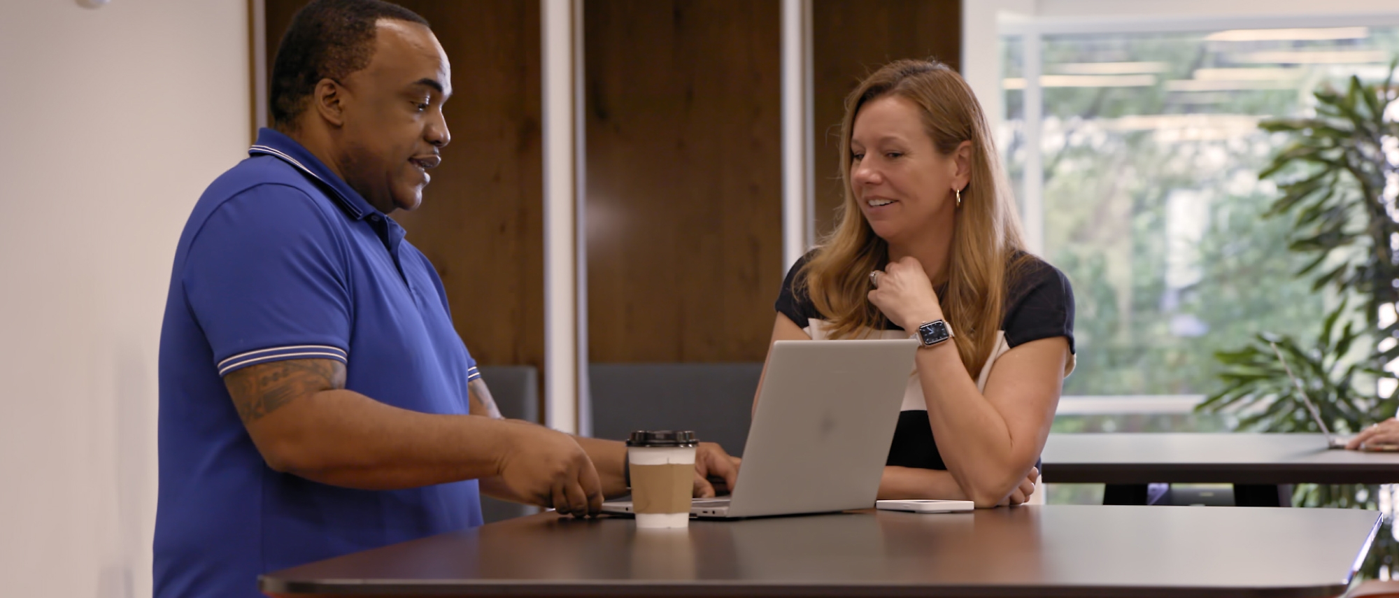 A person and another person sitting at a table with a computer