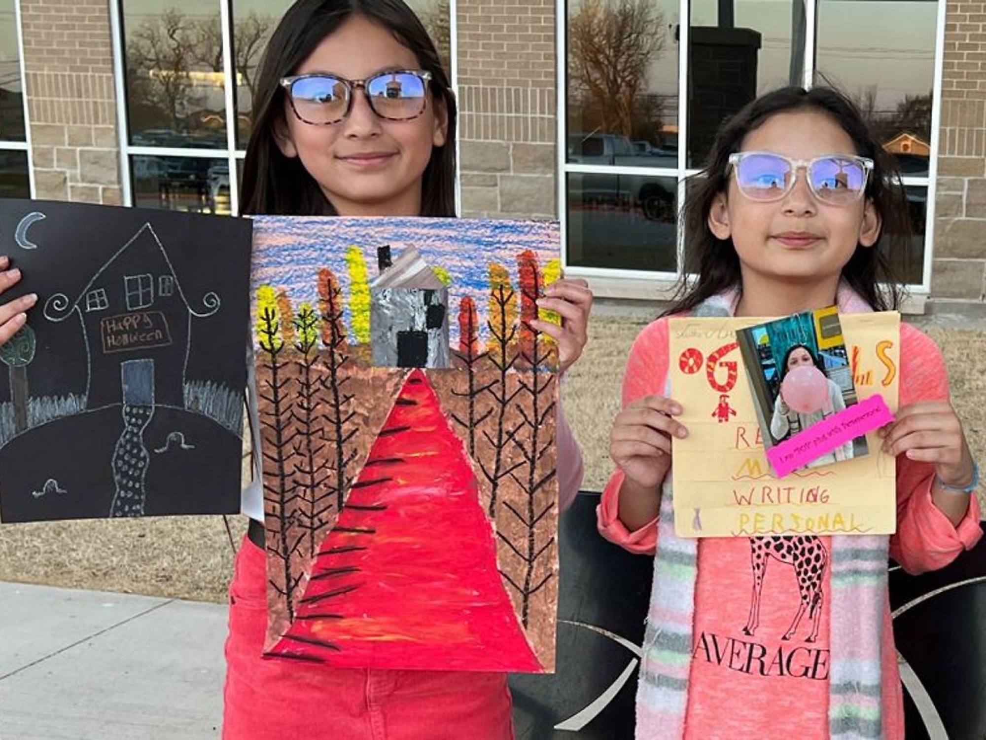 Two girls holding up their paintings.