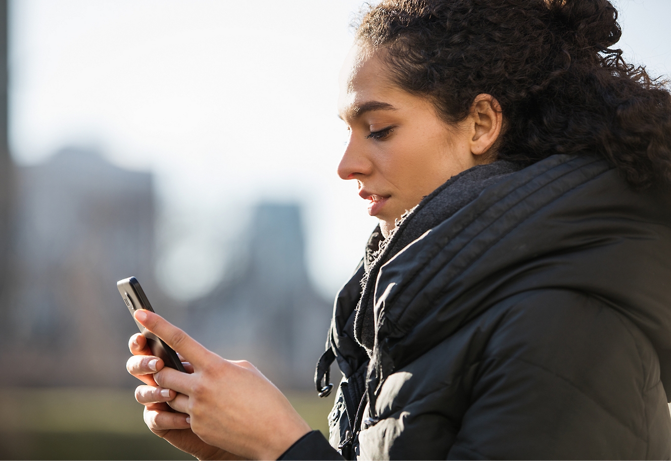 Jauna mergaitė žiūri į savo mobilųjį telefoną