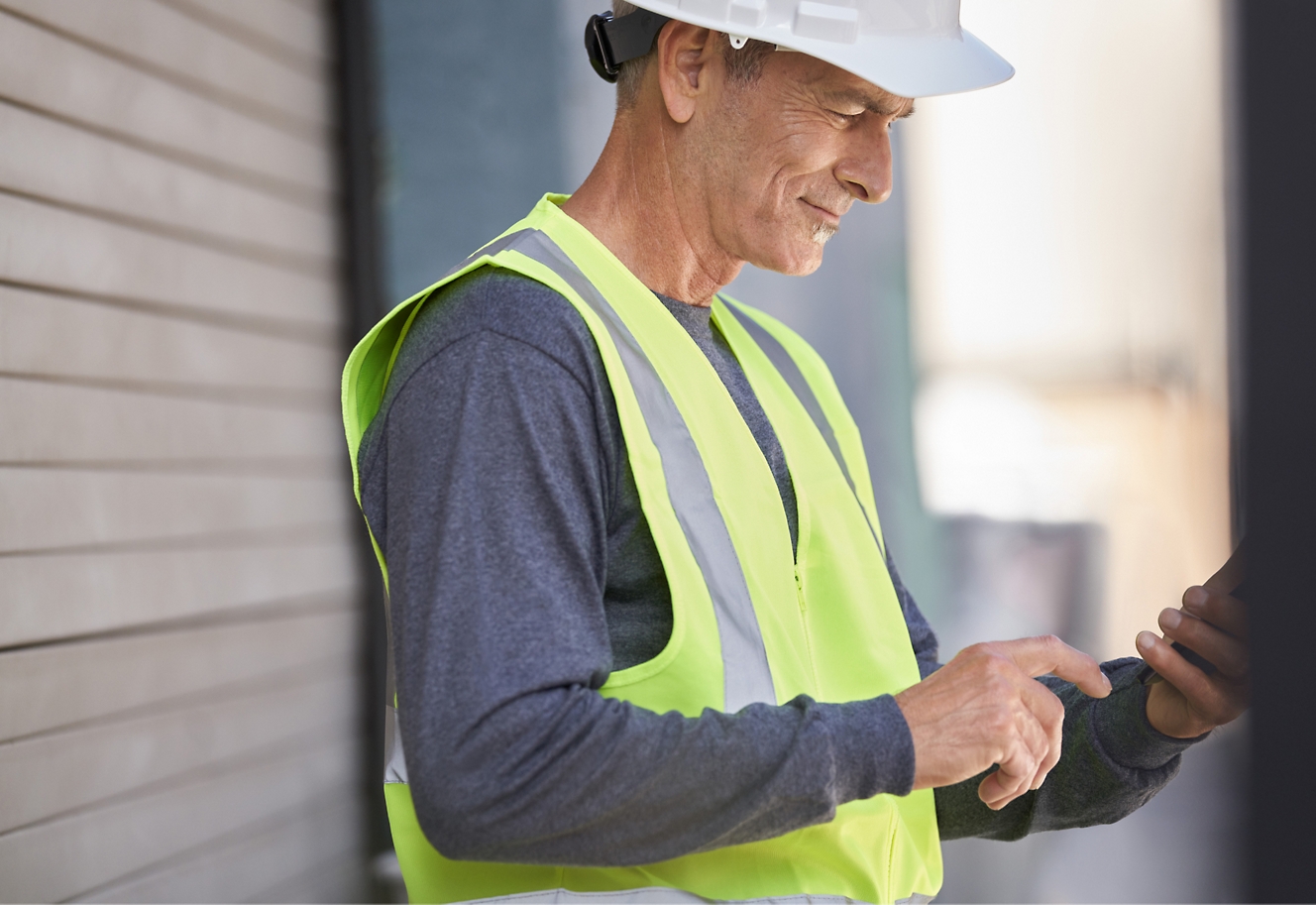 An old men wearing security hat and watching his mobile