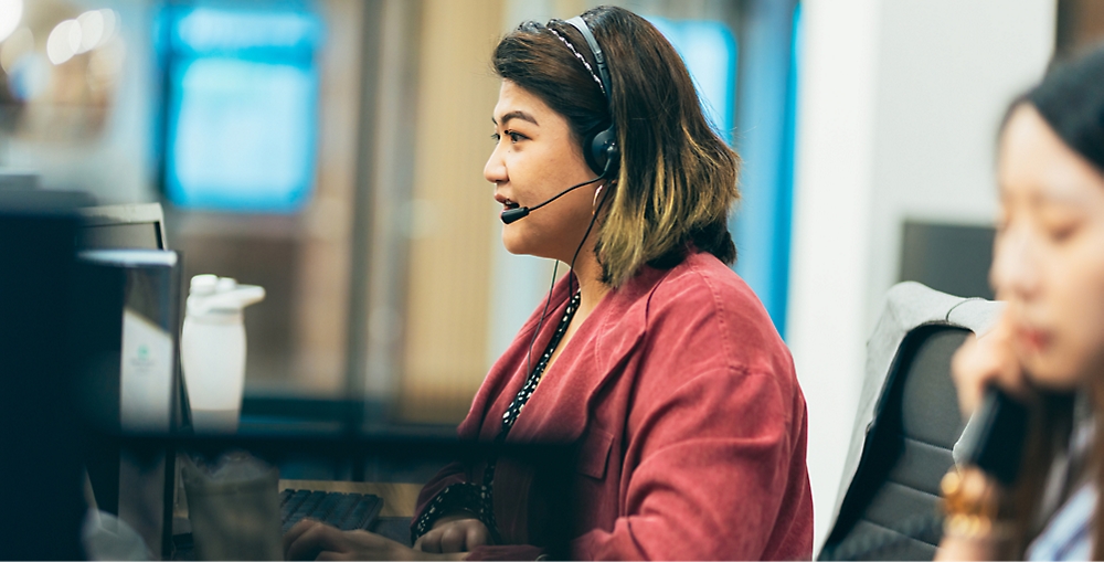 A woman wearing a headset sits at a workstation, focusing on her computer screen.